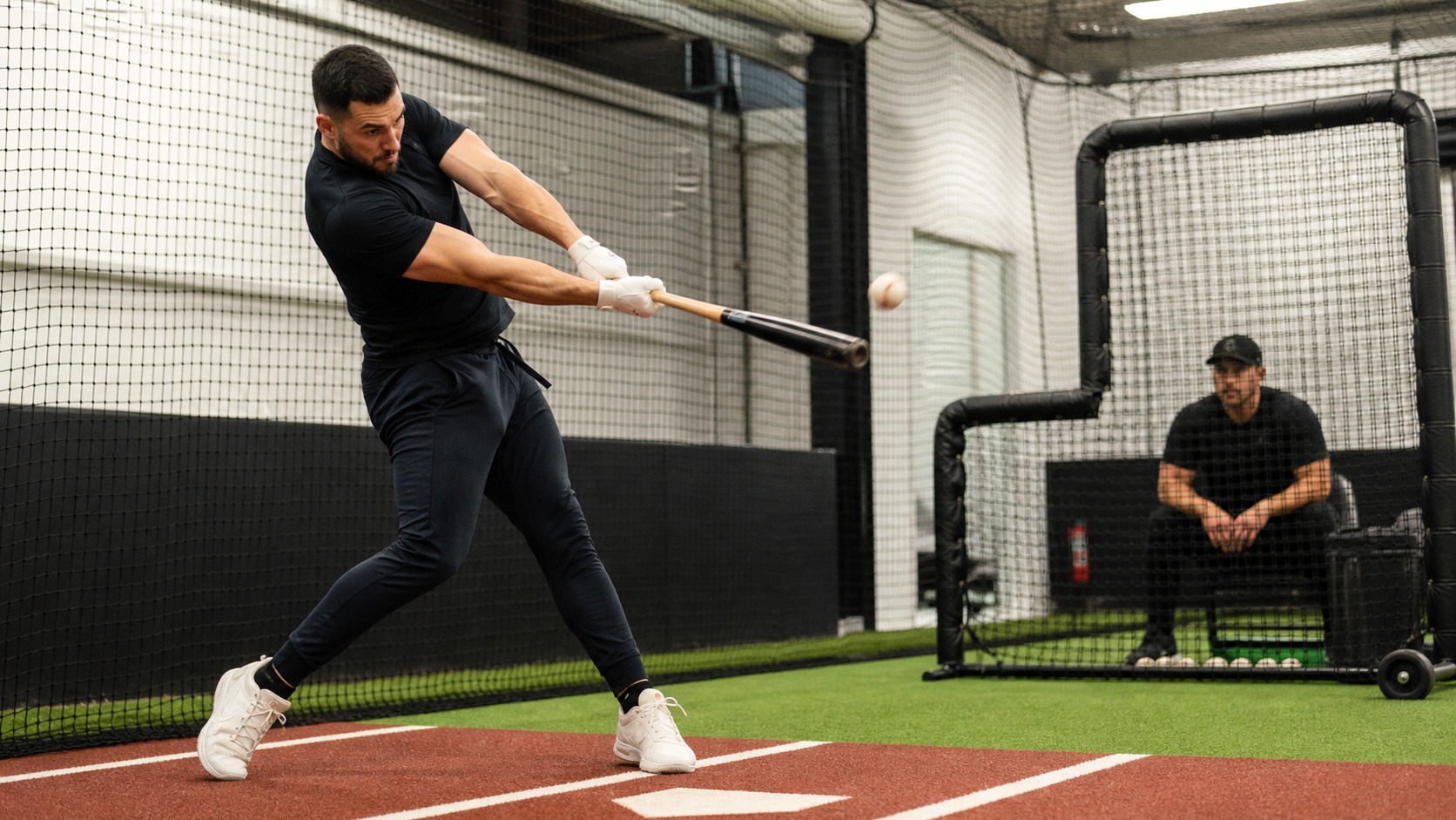 Baseball hitter making strong contact in a batting cage with the ball leaving the bat sharply