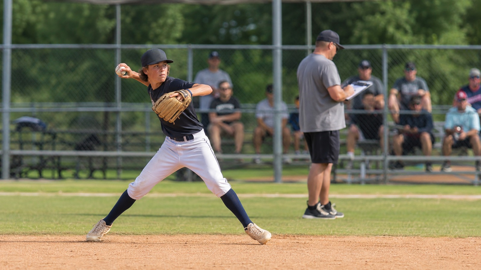 Young baseball player throwing during a showcase-style practice while a coach evaluates from nearby